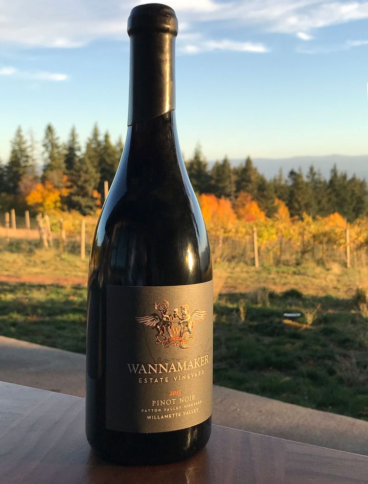 A bottle of Wannamaker wine on a railing above the vineyard at sunset